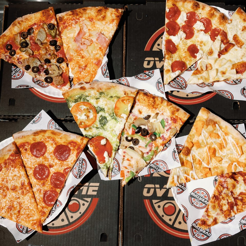 Assortment of Overtime Pizza slices with various toppings, including pepperoni, olives, and pineapple.