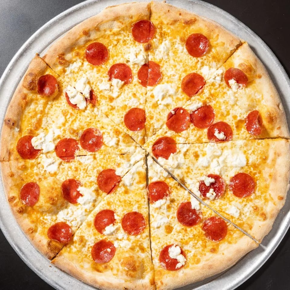Overhead view of a sliced pepperoni and ricotta pizza on a metal pan.