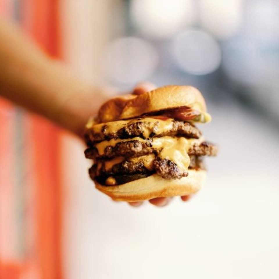 Hand holding a triple-patty cheeseburger with melted cheese on a toasted bun.