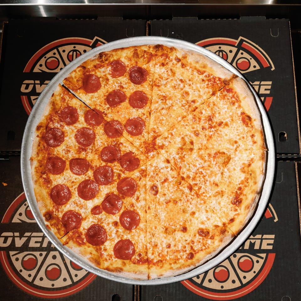 A half pepperoni, half cheese pizza on a metal pan, resting on Overtime Pizza boxes.