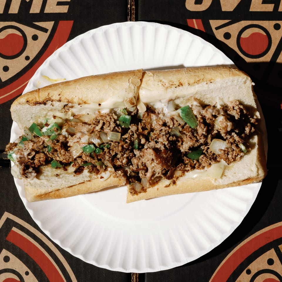 A cheesesteak sandwich with meat, onions, and green peppers on a white paper plate.